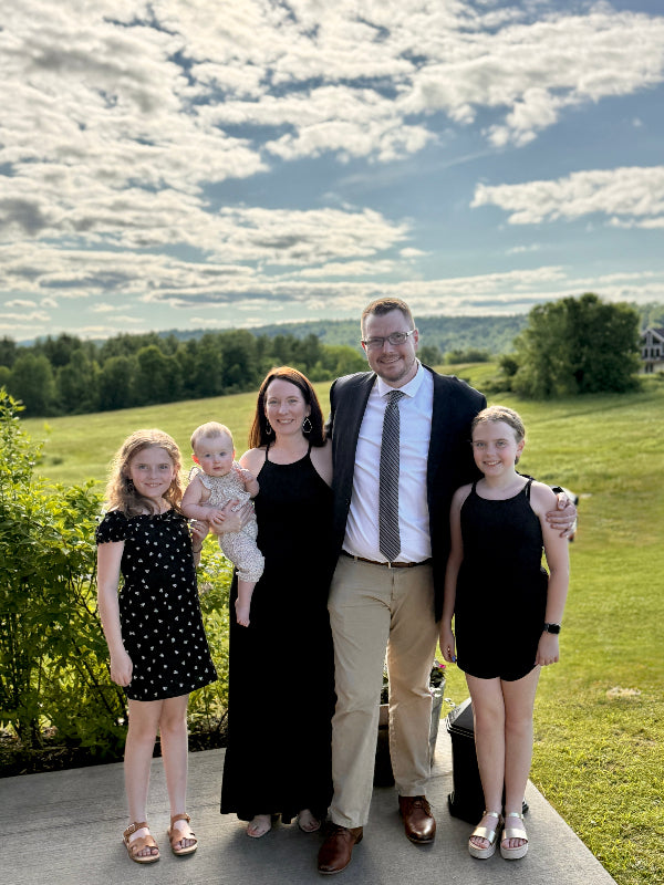 Family of five posing outdoors with a scenic background