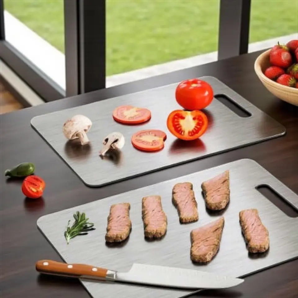 Two metal cutting boards with sliced vegetables and meat on a wooden table.