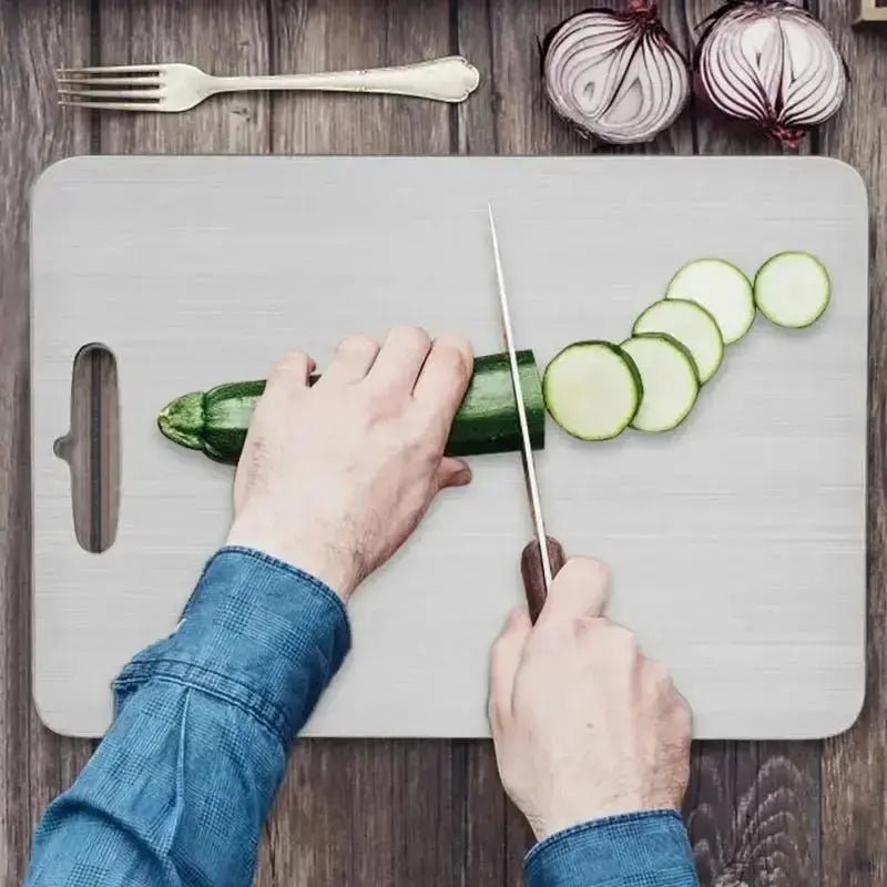 Handpicked Hub stainless steel prep and carving board being used to slice zucchini. Features a built-in handle and knife-friendly surface.